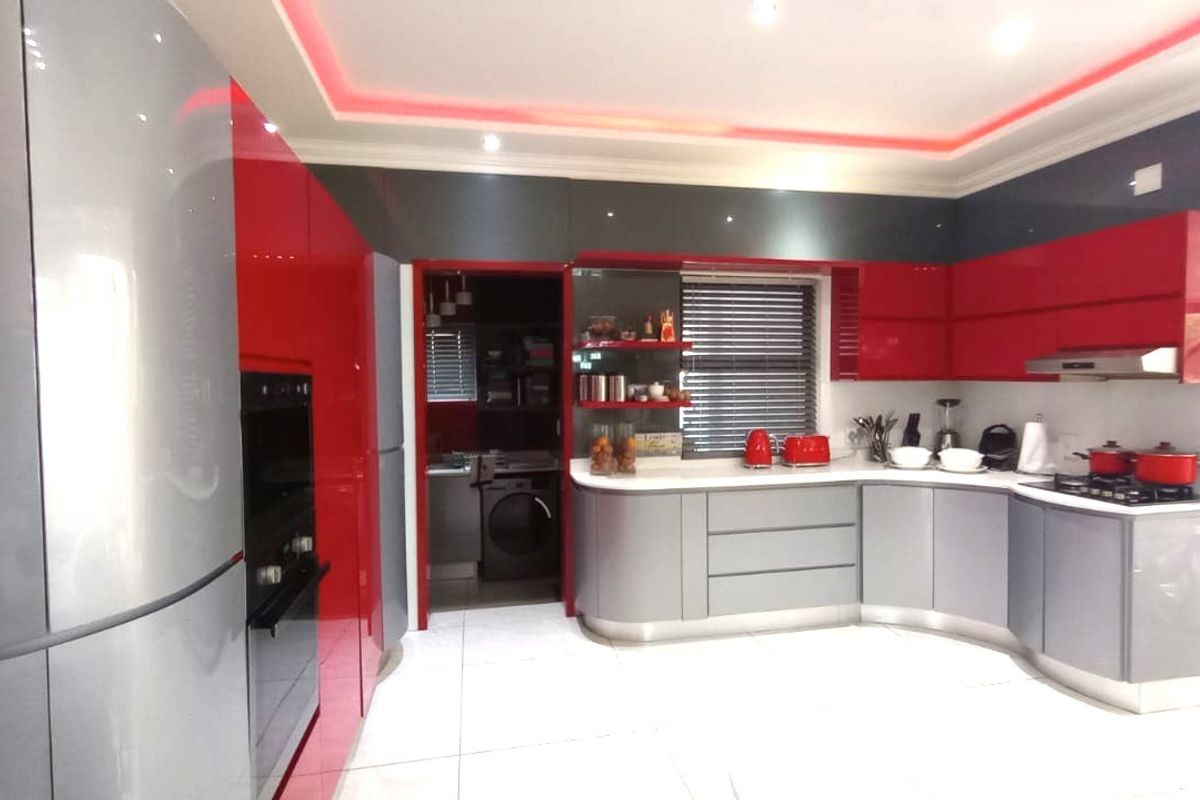 Modern kitchen featuring high-gloss red and grey cabinetry, built-in oven, gas hob, and integrated lighting, with an adjacent scullery area.