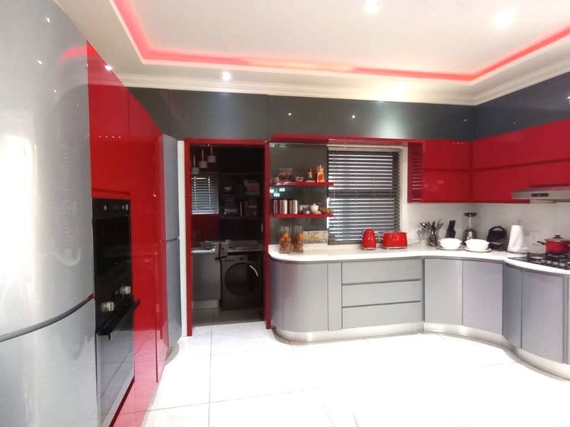 Modern kitchen featuring high-gloss red and grey cabinetry, built-in oven, gas hob, and integrated lighting, with an adjacent scullery area.