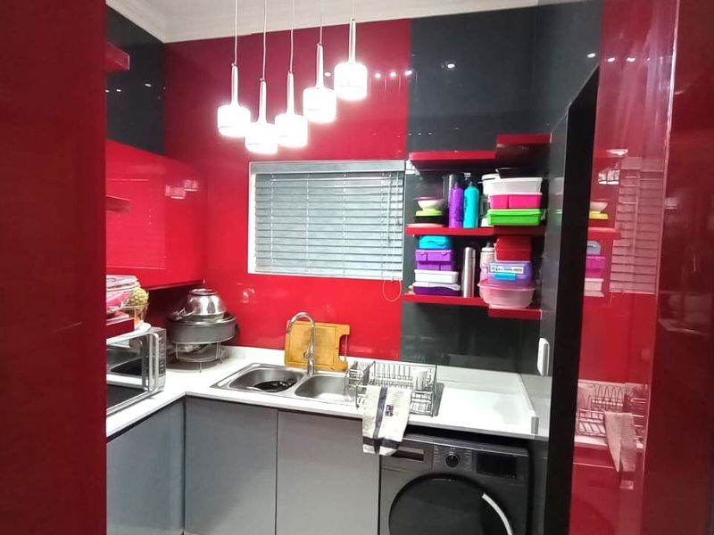 A compact scullery featuring high-gloss red and grey cabinetry, a double bowl sink, and an integrated washing machine with modern pendant lighting.