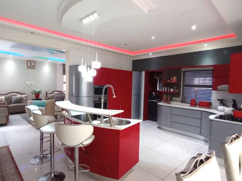 Modern open-plan kitchen featuring high-gloss red and grey cabinetry, a curved breakfast island with integrated sink, and sophisticated recessed and cove lighting.