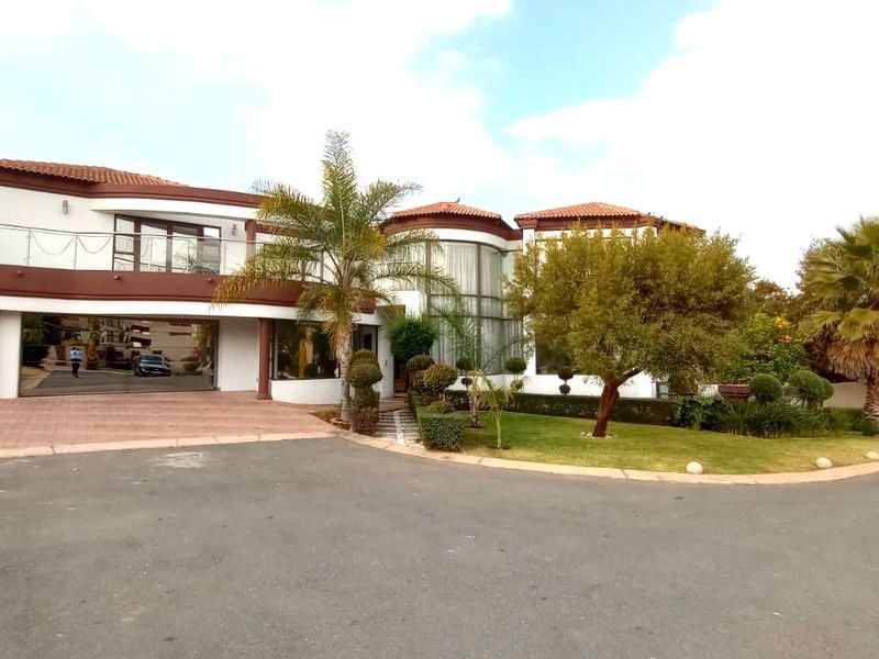 A well-maintained double-story residential property featuring a tiled roof, balcony with glass balustrade, paved driveway, and established landscaped garden.