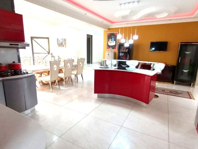 Spacious open-plan kitchen and dining area featuring a curved red kitchen island, modern cabinetry, built-in appliances, and contemporary recessed ceiling lighting.