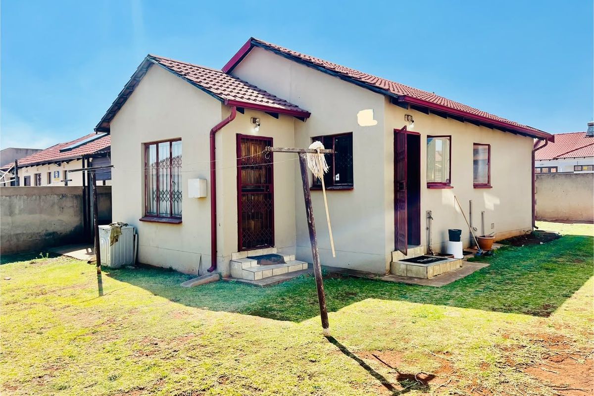 Rear view of a detached house featuring a tiled roof, security-fitted doors and windows, and a private garden area with perimeter walling.