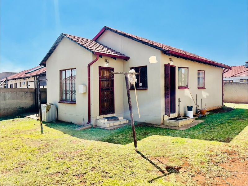 Rear view of a detached house featuring a tiled roof, security-fitted doors and windows, and a private garden area with perimeter walling.