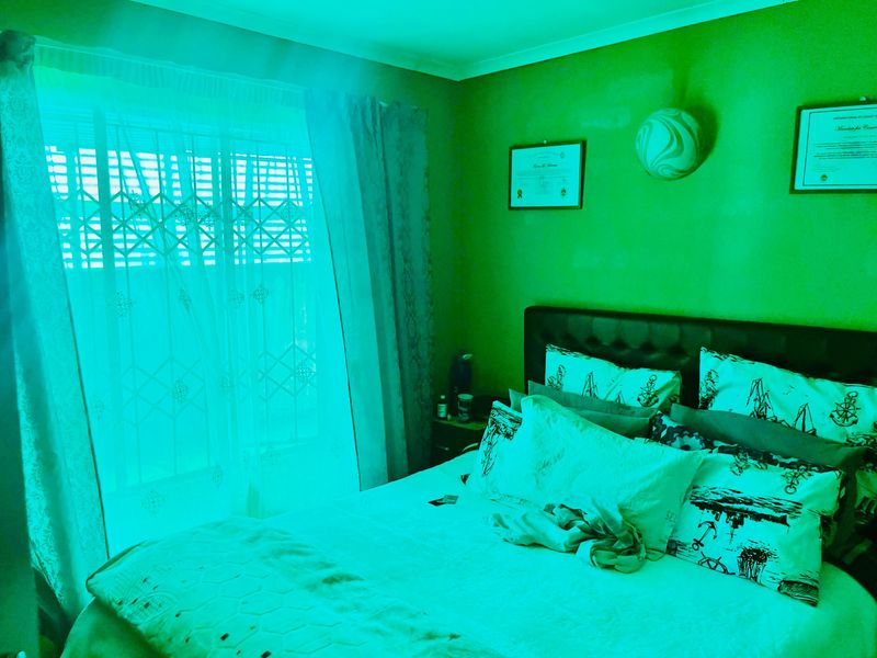 A bedroom interior featuring a window with curtains and wall-mounted lighting, heavily impacted by an unnatural green light cast.