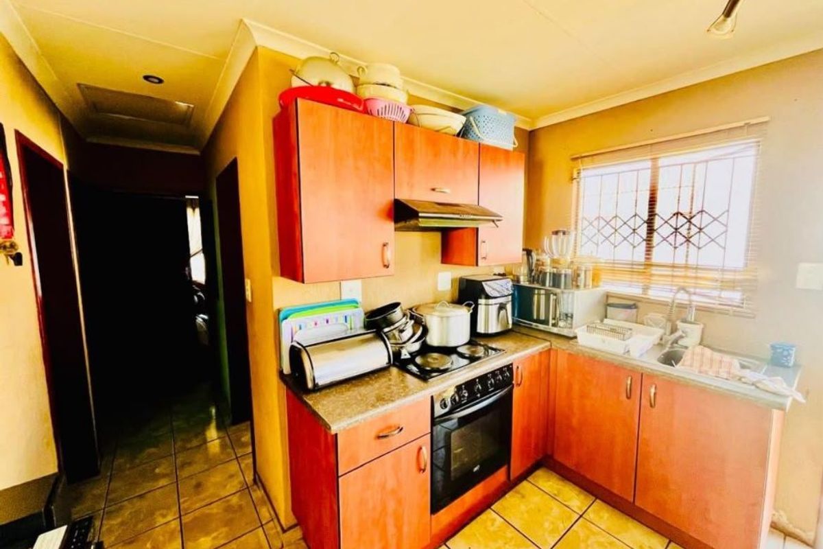 A functional kitchen featuring wood-look cabinetry, built-in oven and hob, tiled flooring, and a window with security bars.