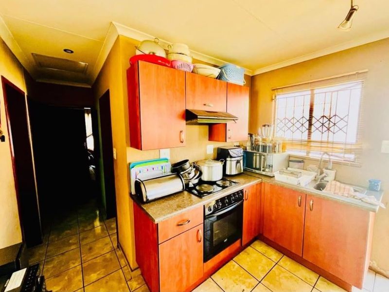 A functional kitchen featuring wood-look cabinetry, built-in oven and hob, tiled flooring, and a window with security bars.