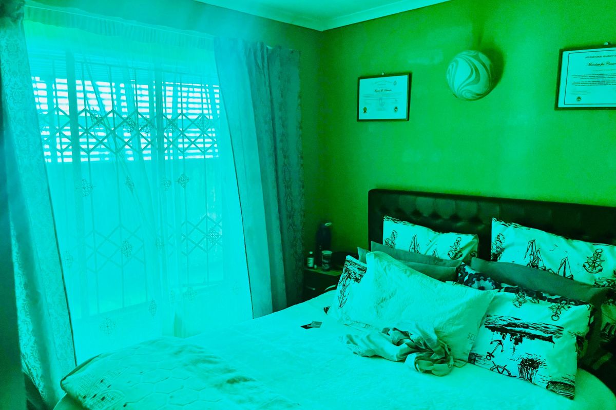 A bedroom interior featuring a window with curtains and wall-mounted lighting, heavily impacted by an unnatural green light cast.