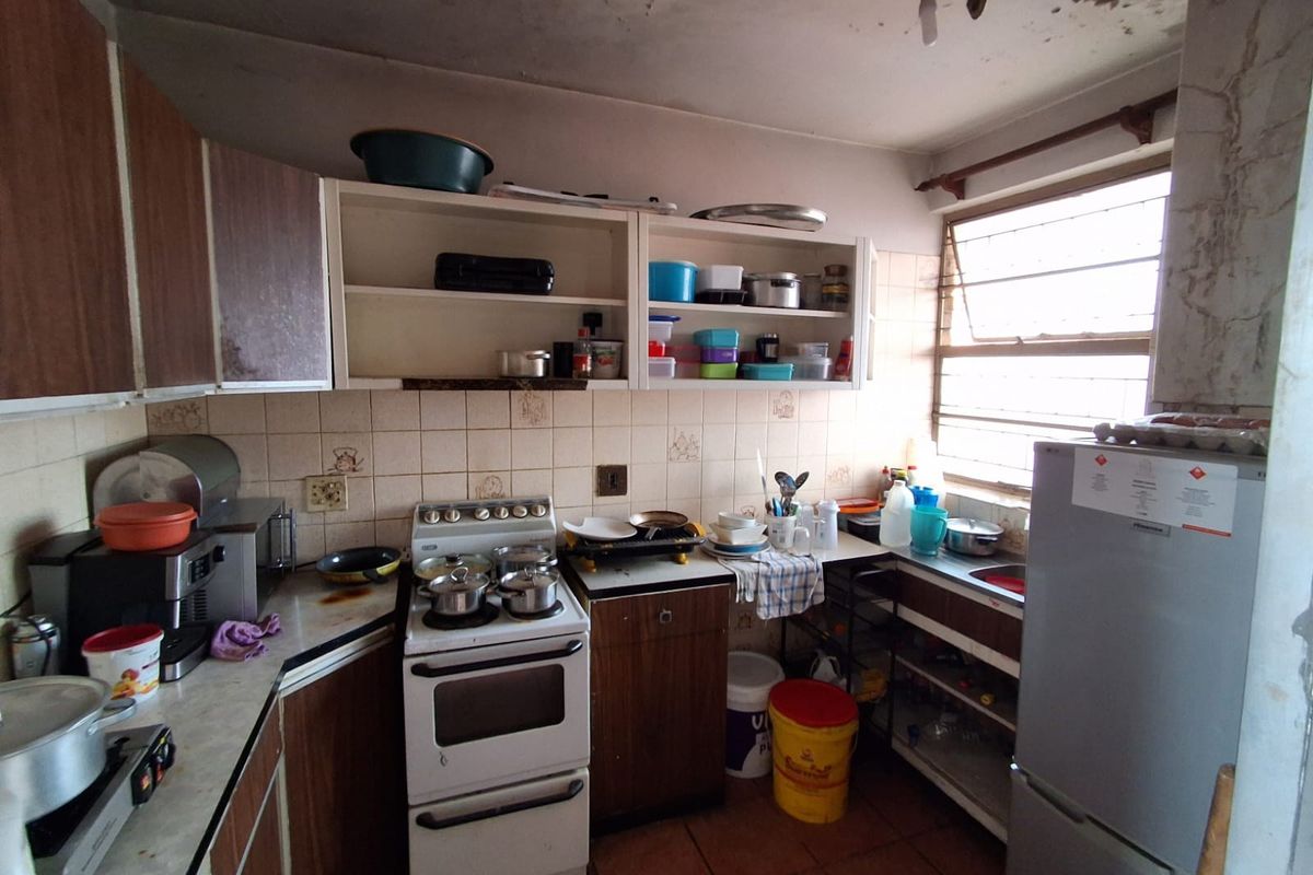 A dated kitchen featuring original cabinetry, a freestanding stove, and a tiled backsplash, currently showing significant signs of wear and ceiling water damage.