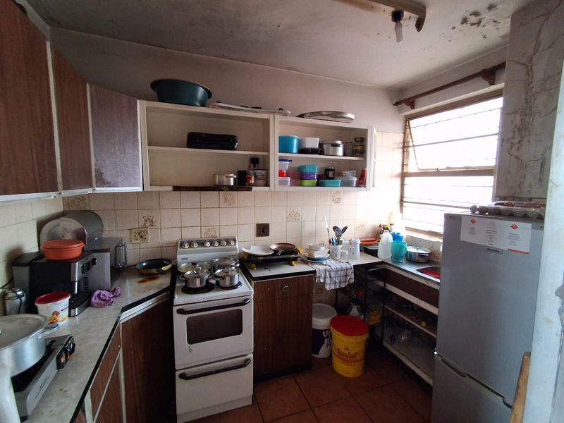 A dated kitchen featuring original cabinetry, a freestanding stove, and a tiled backsplash, currently showing significant signs of wear and ceiling water damage.