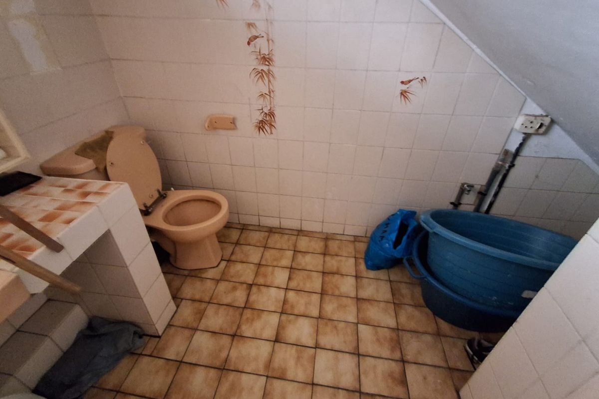 A dated bathroom featuring tiled walls and flooring, a built-in vanity base, and a standard toilet, requiring modernization and cosmetic updates.