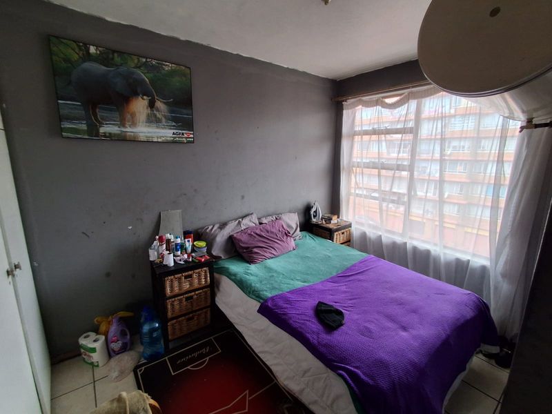 A bedroom featuring tiled flooring and a large window. The room requires cosmetic updates, including fresh wall paint to improve the overall aesthetic.