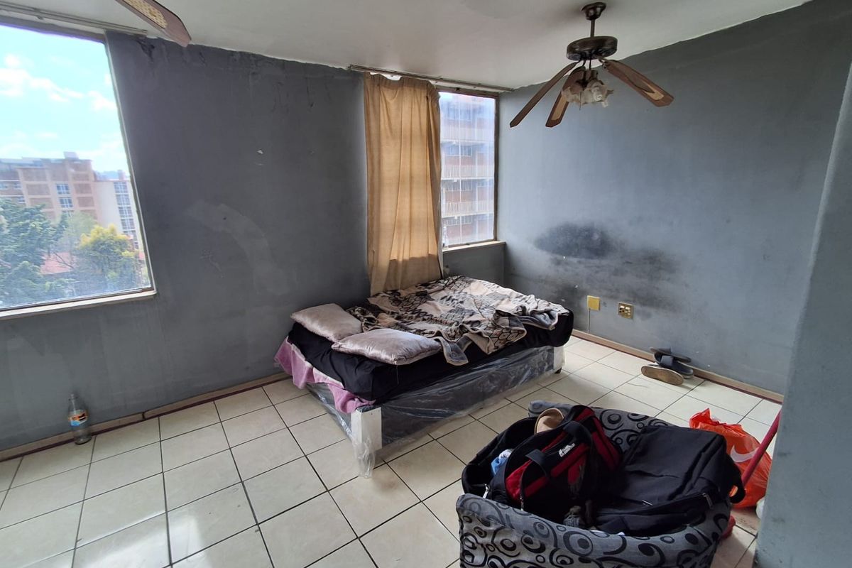 A bedroom featuring tiled flooring and a ceiling fan, currently showing significant wall surface wear and staining requiring maintenance and cosmetic updates.