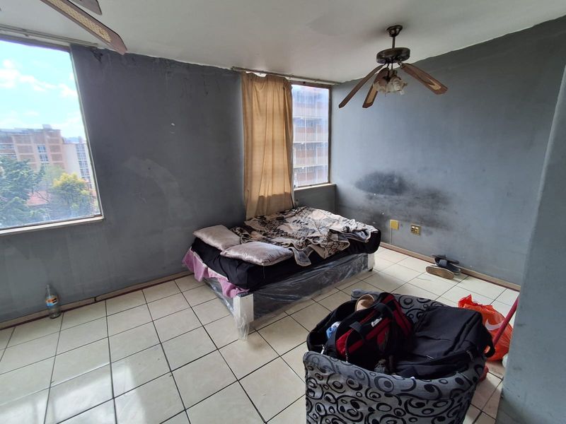 A bedroom featuring tiled flooring and a ceiling fan, currently showing significant wall surface wear and staining requiring maintenance and cosmetic updates.