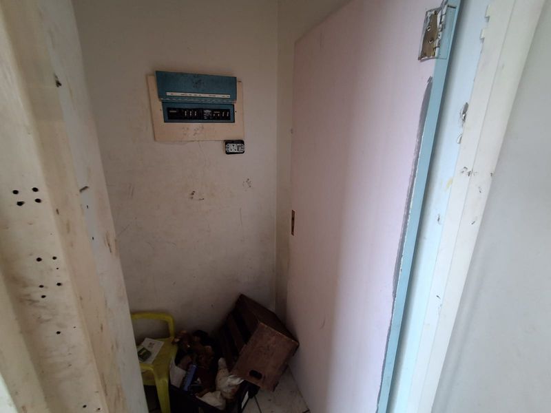 A small utility space featuring an exposed electrical distribution board, requiring cosmetic repairs and maintenance to the walls and door frame.