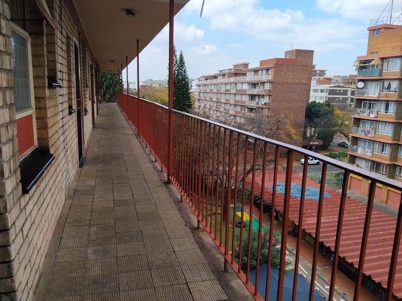 An open-air apartment balcony featuring paved flooring and a metal balustrade, offering an elevated view of the surrounding urban residential area.