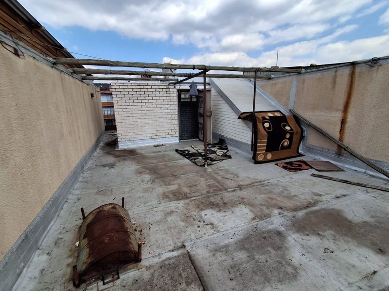 An open-air rooftop terrace featuring a weathered timber pergola frame and concrete flooring, requiring significant maintenance and refurbishment to improve its utility.