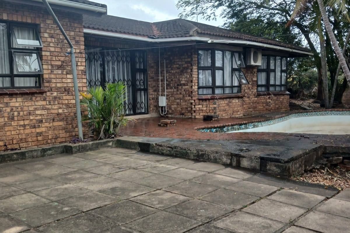 Rear exterior view of a brick house featuring a paved patio area and an in-ground swimming pool.