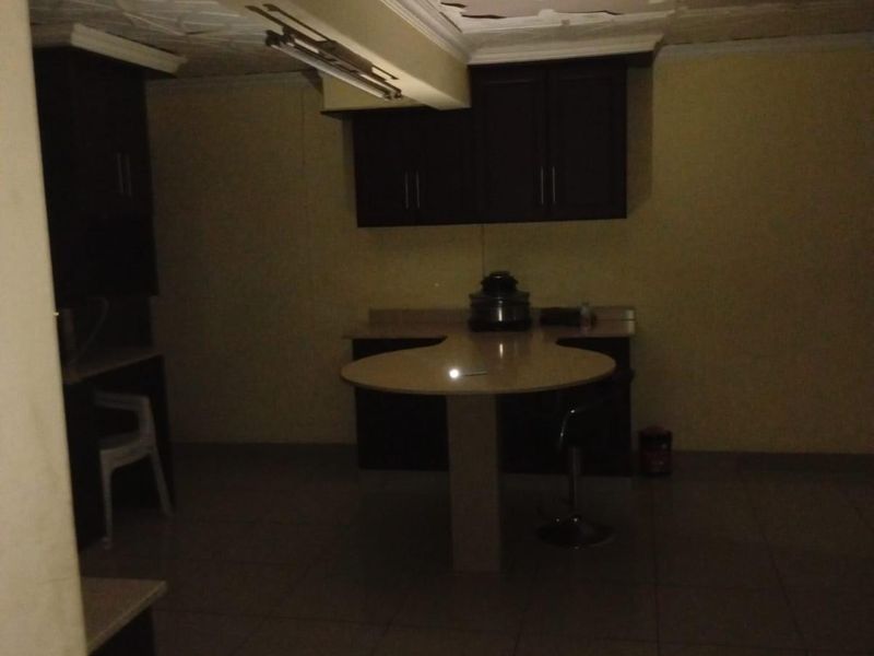 A dimly lit kitchen featuring dark built-in cabinetry, a central counter, and tiled flooring, currently requiring ceiling repairs and improved lighting.