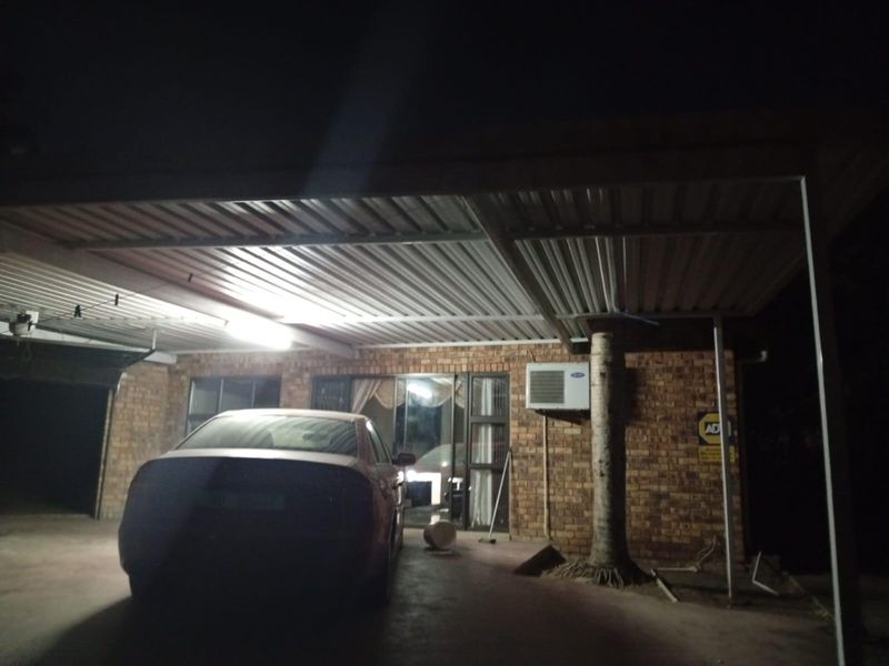 A covered outdoor patio area featuring exposed brick walls, a corrugated metal roof, and a wall-mounted air conditioning unit.