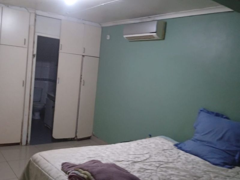 Bedroom featuring built-in cupboards, tiled flooring, and a wall-mounted air conditioning unit, with an adjoining en-suite bathroom visible.