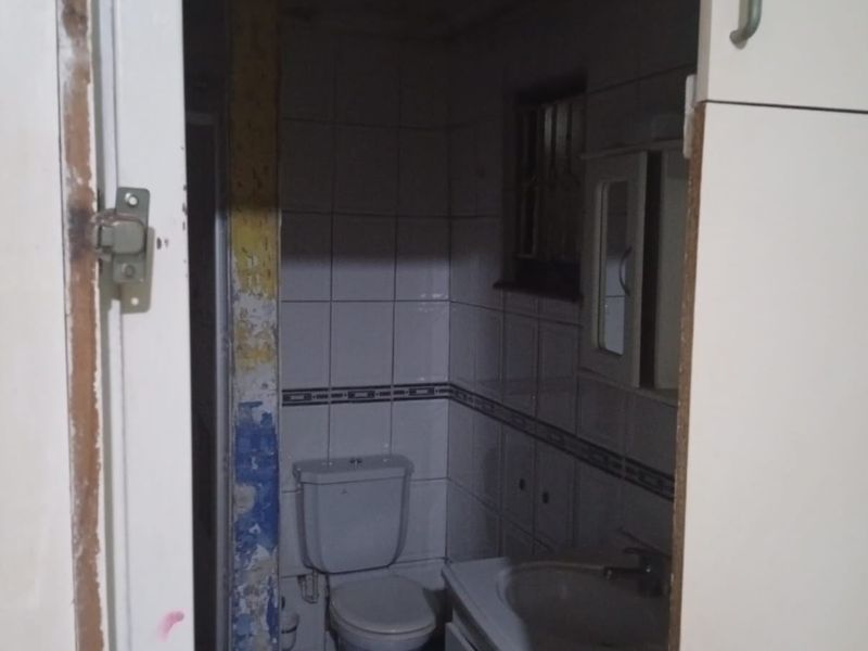 A small, dated bathroom featuring a toilet, vanity basin, and tiled walls, currently in need of cosmetic renovation and improved lighting.