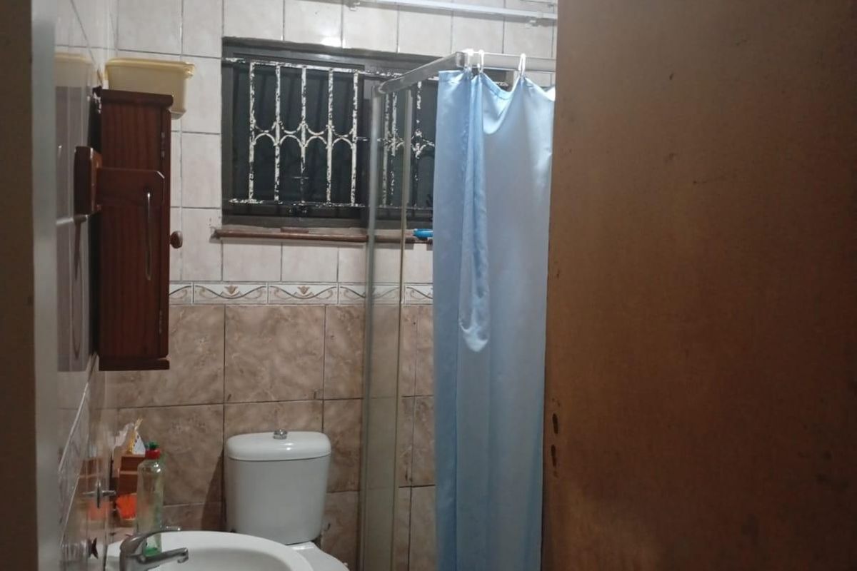 A dated bathroom featuring a pedestal basin, toilet, and shower enclosure, currently requiring significant ceiling repairs and cosmetic updates to improve its condition.
