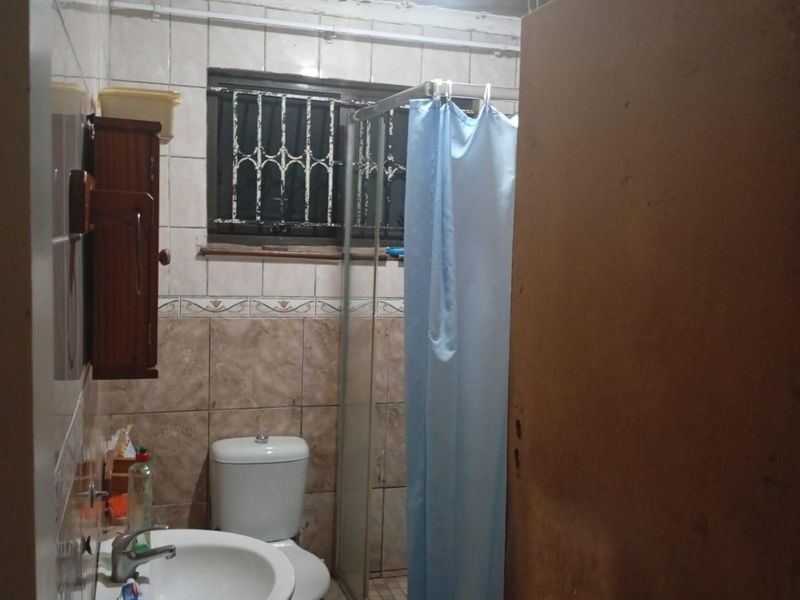 A dated bathroom featuring a pedestal basin, toilet, and shower enclosure, currently requiring significant ceiling repairs and cosmetic updates to improve its condition.