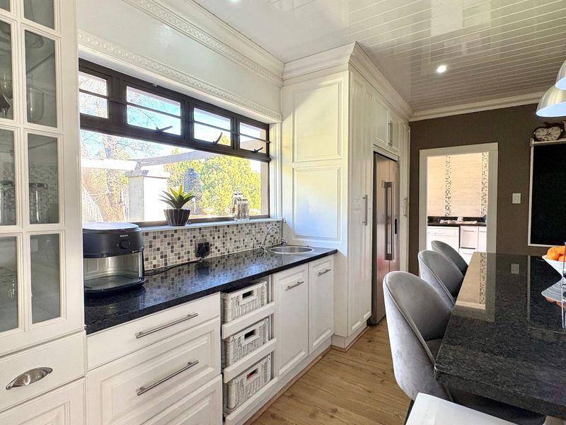 A well-appointed kitchen featuring white cabinetry, dark granite countertops, a mosaic backsplash, and a central island, with a view into an adjacent scullery area.