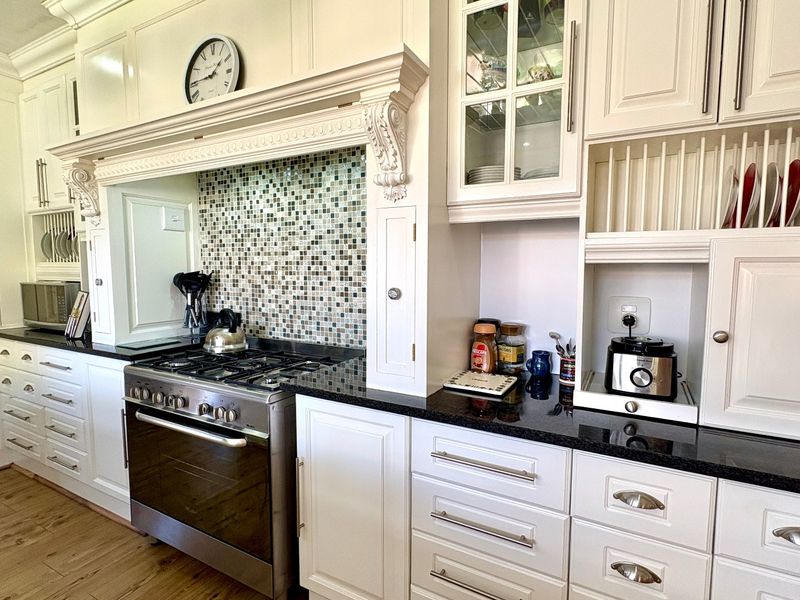 A well-appointed kitchen featuring white cabinetry, granite countertops, a mosaic tile backsplash, and a professional-style gas stove with an integrated extractor hood.