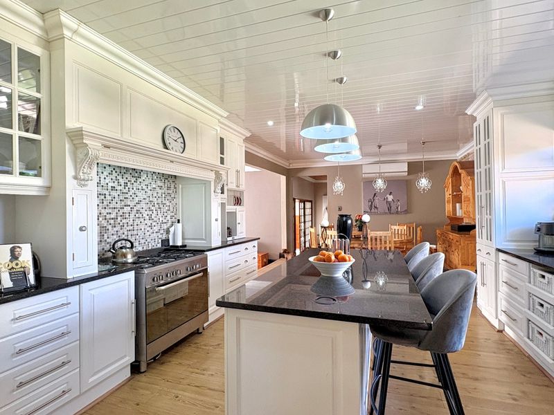 A spacious, well-appointed kitchen featuring a large central island with granite countertops, high-end cabinetry, and a professional-style gas range with a mosaic backsplash.