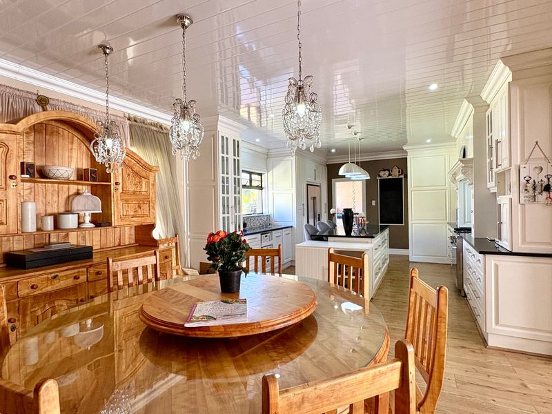 Spacious open-plan kitchen and dining area featuring custom cabinetry, a central island, glossy ceiling finishes, and elegant pendant lighting throughout.