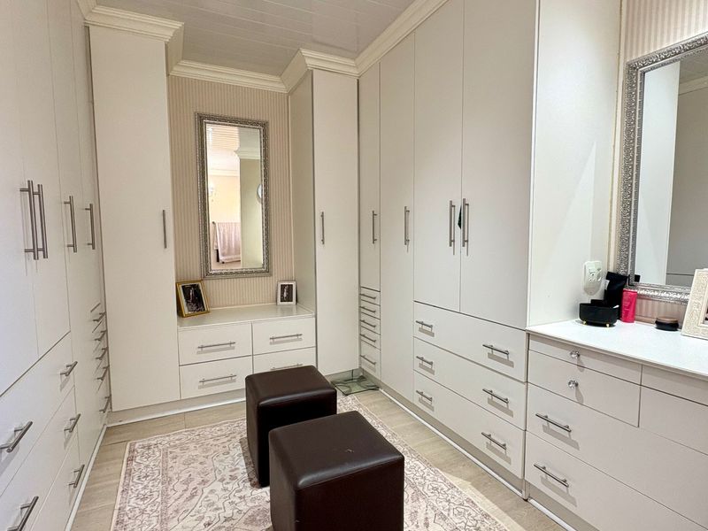 A well-appointed dressing room or walk-in closet featuring extensive white built-in cabinetry, integrated drawer storage, and a dedicated vanity area with a mirror.