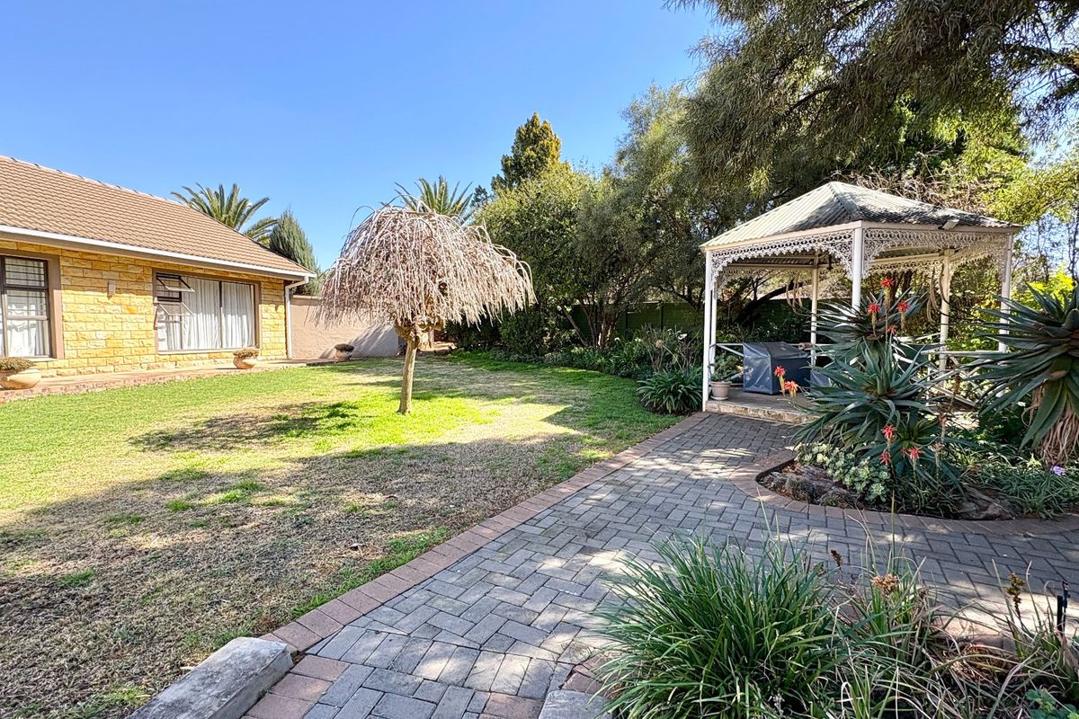 A spacious rear garden featuring a paved walkway, a decorative gazebo, and a well-maintained lawn area adjacent to the main house structure.