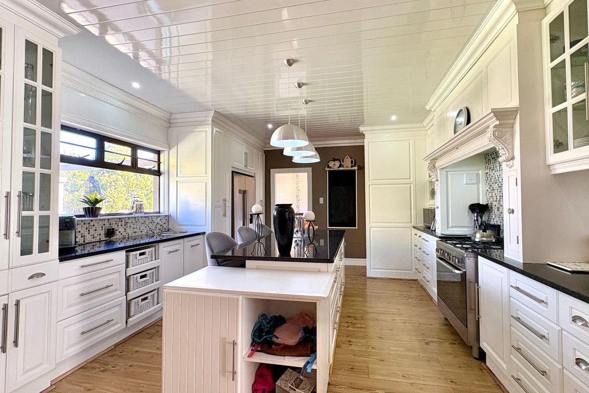 Spacious, well-appointed kitchen featuring white cabinetry, a large central island with granite countertops, high-end gas stove, and elegant tongue and groove ceiling finishes.