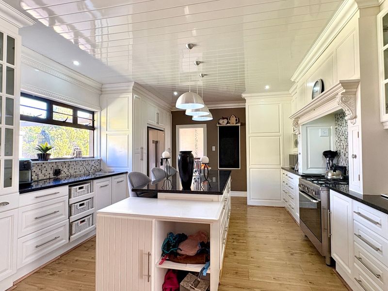 Spacious, well-appointed kitchen featuring white cabinetry, a large central island with granite countertops, high-end gas stove, and elegant tongue and groove ceiling finishes.