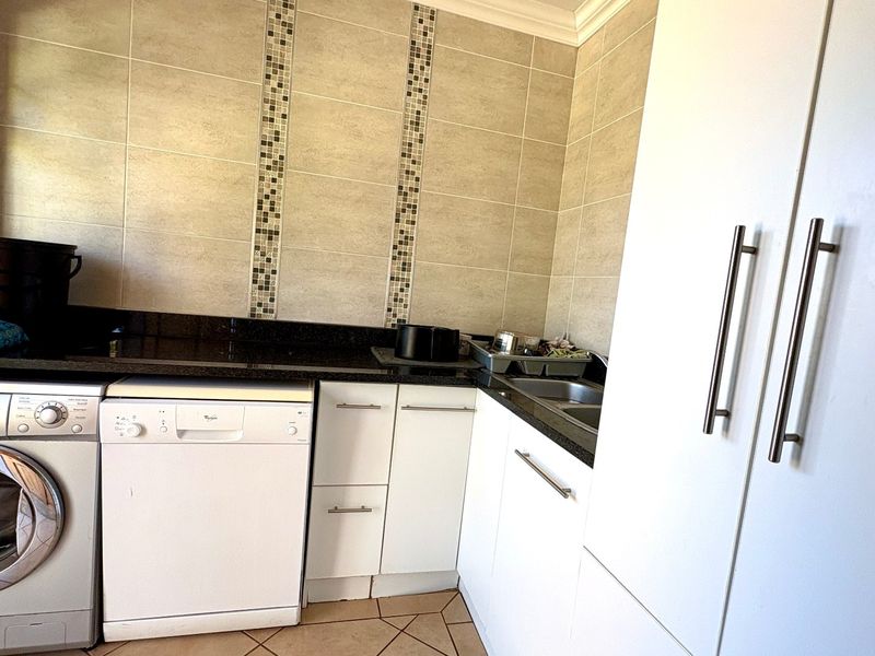 A functional laundry room featuring granite countertops, built-in white cabinetry, a stainless steel sink, and tiled wall accents.