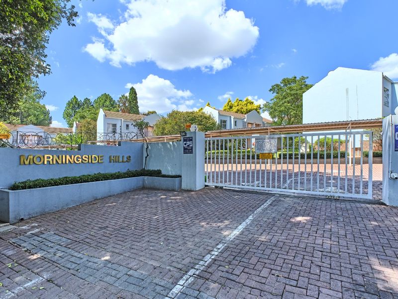 The entrance to Morningside Hills apartment complex featuring a secure gated access point, paved driveway, and perimeter wall with electric fencing.