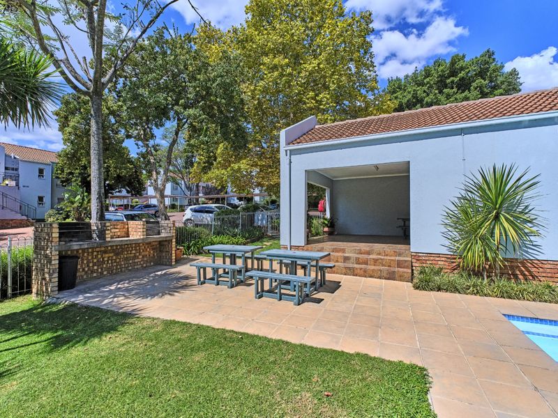 Outdoor entertainment area featuring a swimming pool, covered patio, and a built-in brick braai, set within a landscaped communal garden.