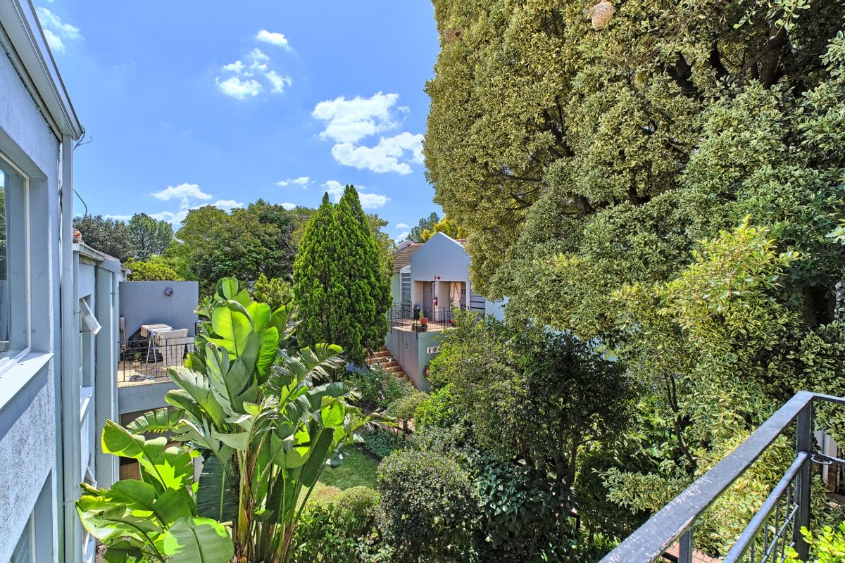 A view from an elevated balcony overlooking a lush, mature garden and surrounding residential property structures.