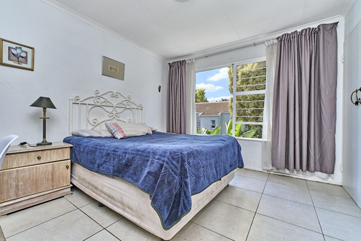 A functional bedroom featuring tiled flooring and a large window with curtain tracks, offering natural light and a view of the surrounding area.