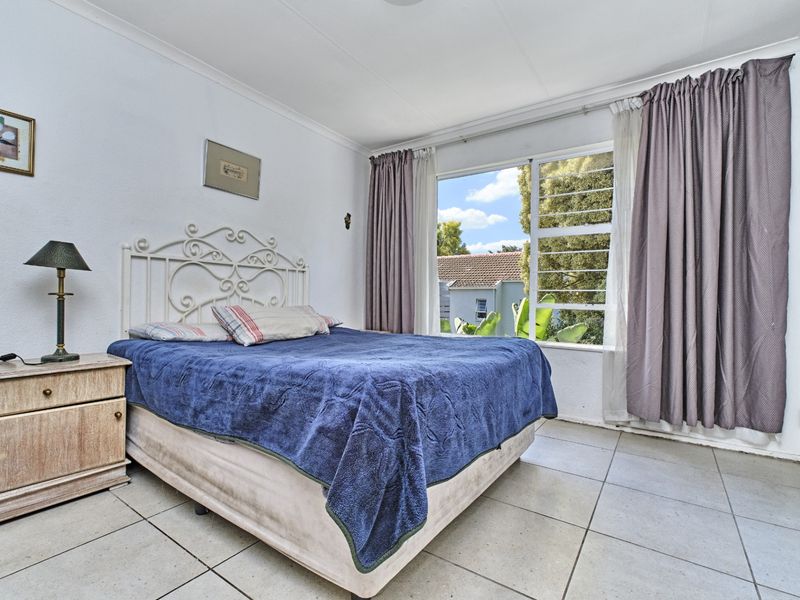 A functional bedroom featuring tiled flooring and a large window with curtain tracks, offering natural light and a view of the surrounding area.