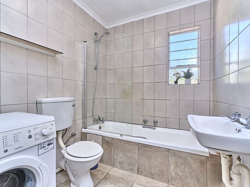 A functional bathroom featuring a bathtub with a glass screen, pedestal basin, toilet, and tiled finishes, including space for a washing machine.