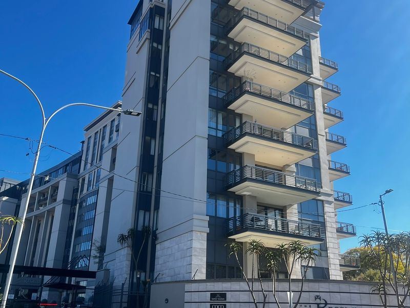 A modern multi-story apartment building featuring stacked balconies, stone facade detailing, and a secure entrance area.