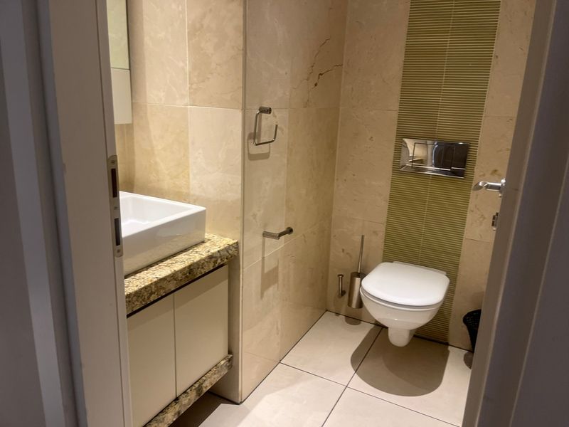 A modern bathroom featuring a wall-mounted toilet, granite vanity countertop with a vessel sink, and neutral stone-tiled walls with a decorative accent strip.
