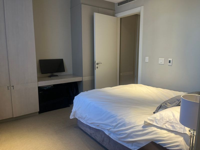 A functional bedroom featuring built-in cupboards, a dedicated desk area, and neutral carpeting, offering a clean and practical living space.