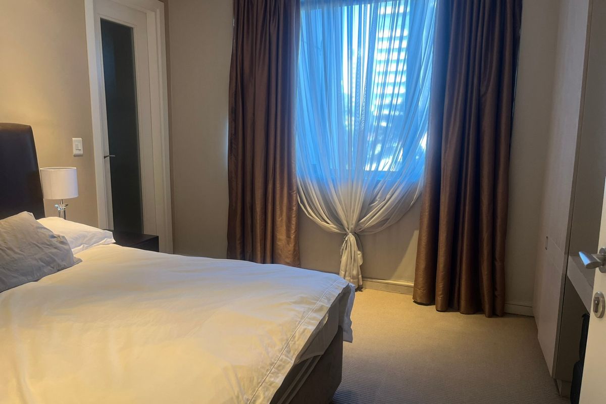 A well-maintained bedroom featuring neutral carpeting, built-in storage, and large windows dressed with layered curtains.