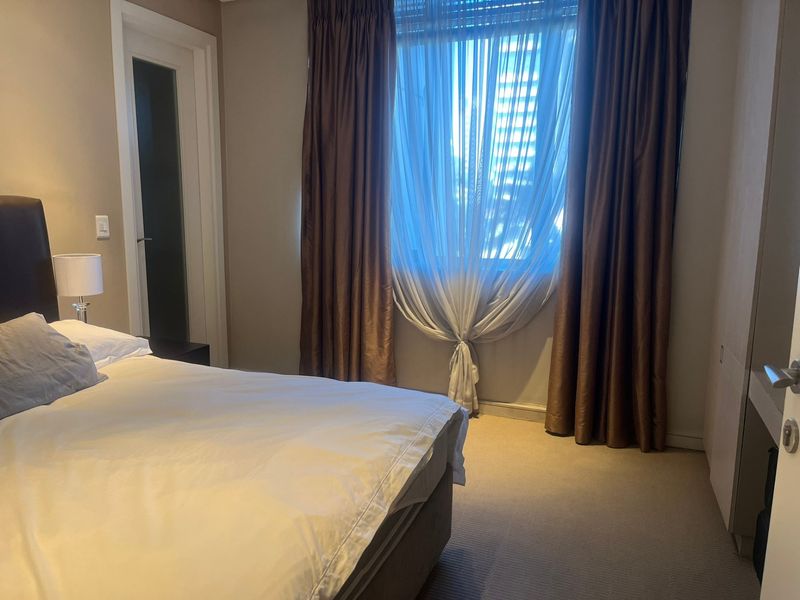 A well-maintained bedroom featuring neutral carpeting, built-in storage, and large windows dressed with layered curtains.