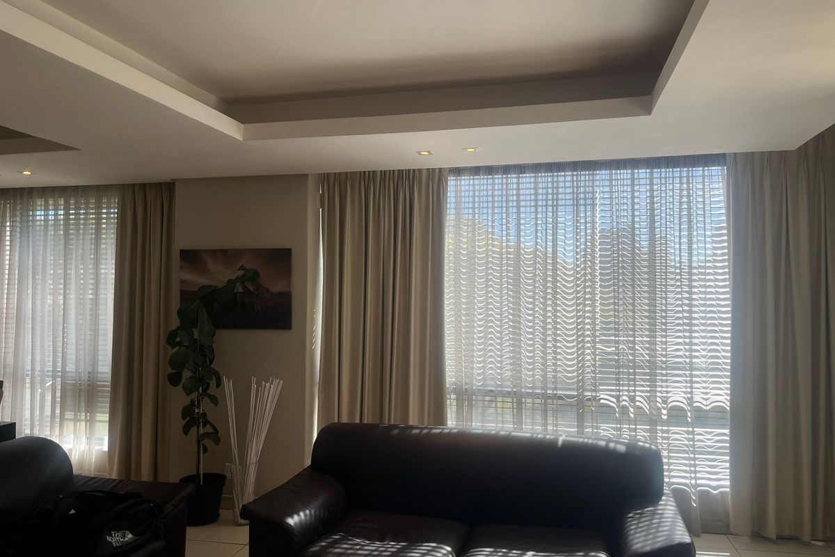 A bright living room featuring a recessed ceiling with integrated downlights and large windows dressed with floor-to-ceiling curtains.