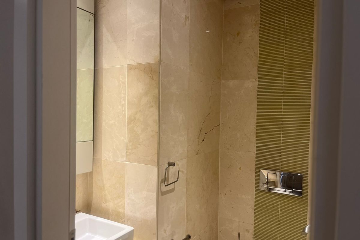 A compact bathroom featuring stone wall tiling, a wall-mounted toilet with a chrome flush plate, and a vessel sink on a stone vanity.